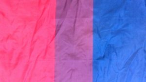 Bi flag, as slightly crumpled fabric flat on a surface. Pink, purple, blue.