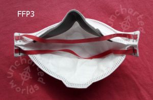FFP3 mask, from the inside, showing the grey foam nose piece. Two red rubber bands go from one side to the other of it, held on by staples.