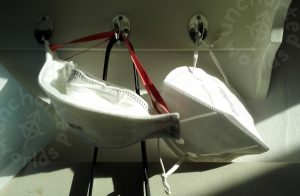 Two disposable masks are hung from little silver-coloured hooks, in bright sunlight. One is an FFP2 type, the other is an FFP3 type.